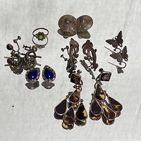 Full lot display showing a variety of vintage sterling silver jewelry including earrings with green and blue stones, tortoise shell chandelier earrings, butterfly clips, and floral designs.