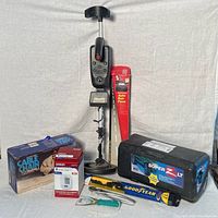 Wide view of all lot items including metal detector, tire chains, blood pressure monitor, auto sun fans, tool, and tire chain packaging