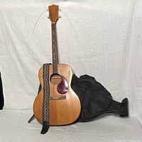Full view of vintage acoustic guitar with colorful patterned strap and black soft case behind