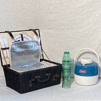 Photo showing the open insulated picnic basket next to stacked green embossed glasses and the Coleman drink cooler.