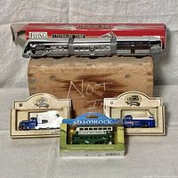 Full lot view showing all toys including the vintage Flying Yankee Streamline train, two blue and white trucks in original display packaging, and a green Shamrock bus model in carded packaging.