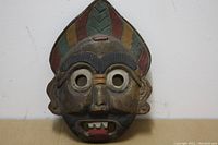 Front view of the carved wooden face mask showing carved facial features and painted colors