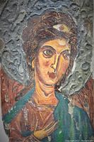 Close-up of painted angel with detailed facial features and halo on wooden panel.