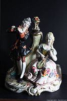 Front view of the porcelain statue showing a couple with the man playing violin and the woman playing a lute or mandolin, detailed hand-painted porcelain with floral decorations