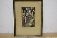 Full view of framed print showing street scene with flowers and donkeys.