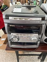 Front view of AIWA audio system showing main unit with display, control buttons, circular jog dial, and volume knob.