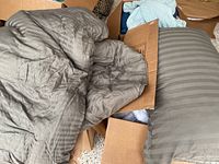 Comforters and pillows with matching gray striped fabric seen partially out of a cardboard box.