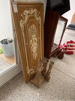 Three decorative candleholders with worn paint finish grouped in front of a large decorative wall art panel leaning against glass door