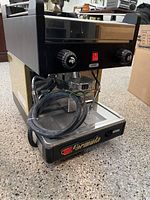 Front view of black and stainless steel Formula cappuccino maker with control knobs, power switch and coiled power cable.