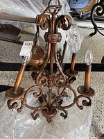 Full view of bronze coated chandelier with four candle-style bulb holders and decorative scrollwork