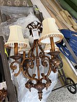Full view of bronze coated chandelier with three cream-colored lampshades with beaded fringe.