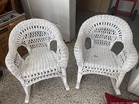 Two white wicker children's rocking chairs side by side showing full frontal view.