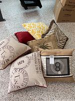 Photo showing seven decorative pillows on a floor including various designs and textures.