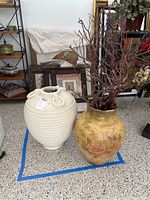 Wide view of two decorative pots side by side on a speckled floor with shelves and framed items in the background.