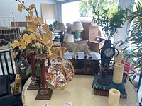 Wide shot showing antique Chinese box, stone elephant, ceramic plates on brass stands, faux florals, candles, books, and clock arranged on a table.