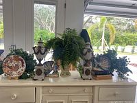 Wide shot of two urns, two peacocks, plates with stands and fern arrangement on white sideboard