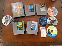 Photo showing NES cartridges (Baseball, Lode Runner), Sega Genesis Alien Storm in case, and PlayStation game discs including Guitar Hero and Rock Band.