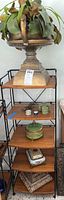 Full shelf view showing large urn planter on top shelf, decorative boxes on lower shelves of metal and wood plant stand.