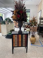 Front view of the bathroom vanity with large faux preserved floral arrangement in dark urn vase on top, and additional large faux floral arrangement nearby in hand-painted ceramic vase.
