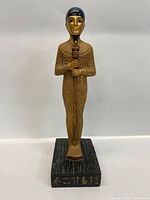 Front view of the Ptah statue showing gold face, textured garment, staff, and base with hieroglyphs.