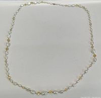 Full view of the necklace laid out flat showing the entire length of alternating white pearlescent and amber faceted beads.