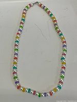 Full view of the custom beaded necklace laid flat showing the alternating pattern of white faux pearls and various colourful disc-shaped beads.