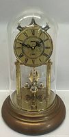 Front view of the entire Gruen anniversary clock showing the glass dome, base, and clock face with Roman numerals and decorative pendulum balls below.
