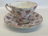 Teacup on matching saucer showing floral cracked glaze pattern with gold trim on rims and handle.