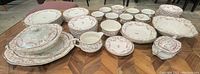 Wide angle photo showing the full set of Alfred Meakin floral china including plates, bowls, cups, covered serving dish, sugar bowl, and platters arranged on a wood parquet floor.