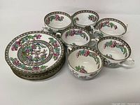 Six floral pattern Coalport plates stacked next to six tea cups including one double handled cup.