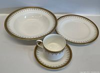 Overall view of the teacup, saucer, and two plates with gold decorative trim and white porcelain.