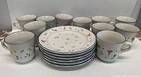 Front view of 8 stoneware tea cups and 8 plates arranged on surface showing floral pattern and blue rim details.