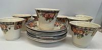 Eight floral patterned tea cups arranged behind a stack of matching saucers, showing the full lot comprising tea cups and saucers in floral and gold decorative style.