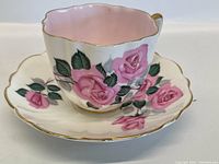 Tea cup with pink rose floral patterns and gold trim on scalloped rim.