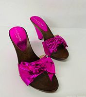 Pair of metallic bright pink ladies high heel shoes with bows and cone-shaped heels shown from top angle