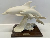 Front view of white dolphin sculpture showing two dolphins jumping over sculpted waves, mounted on wooden base.