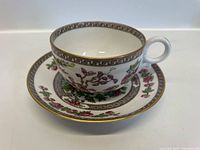Full view of the tea cup placed on top of the matching saucer showing floral designs and gold rim