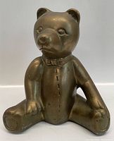 Front view of vintage brass bear piggy bank showing sitting bear with bow tie and facial details.