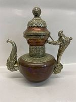 Front view of copper tea pot with ornate silver spout, handle, and decorative lid on top