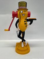 Full view of vintage Mr Peanut peanut butter maker figurine featuring yellow peanut-textured body, black limbs, white gloves and shoes, red crank handles and top hat.
