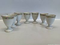 All seven Limoges egg holders arranged in a row showing their shape and floral pattern.