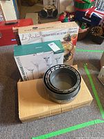 Five nested metal springform cake pans shown on top of a cardboard box, boxed ceramic platters and glass candle holders in background