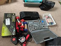 Photo showing the PowerMat wireless charging mat box, ratchet set in carrying case with sockets and wrenches, two small dumbbells, hand grip strengtheners, pens, pencils in white basket, and cassette tapes in black zippered case.