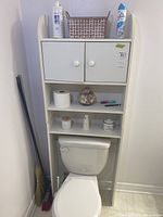 Front view of white laminated wood cupboard over toilet with items on shelves and cabinet doors closed.
