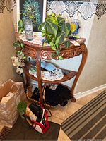 Front view showing demi-lune table with carved wood apron, two levels and stone top, with decorative plants and items on and around it.