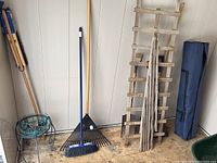 Photo of broom, rake, garden loppers, wooden trellises, green metal plant stand, and blue carrying case for foldable gazebo.
