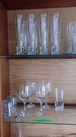 Top shelf with six tall clear glass champagne flutes, bottom shelf with three stemmed wine glasses and three cylindrical water glasses.
