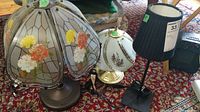 View of four lamps showing their bases and shades including the glass floral shade, black fabric shade, and the taller lamp without shade