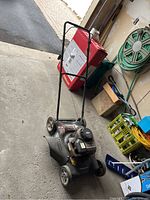 Full side view of the lawn mower showing engine, wheels, and handlebar in garage setting.