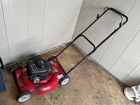Full side view of the red Murray lawn mower with black handlebars on a wooden floor.